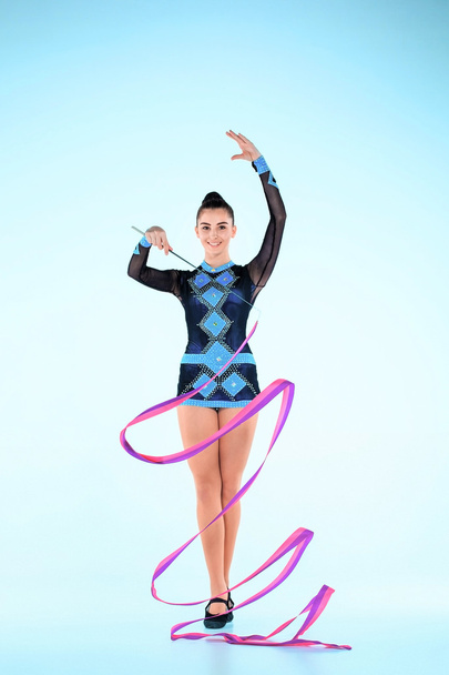 The girl doing gymnastics dance with colored ribbon on a blue background - Фото, зображення