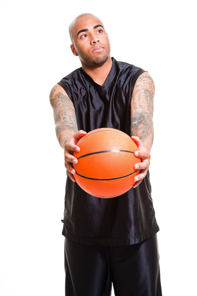 Porträt eines jungen Basketballspielers, der mit einem Ball vor weißem Hintergrund steht. Studioaufnahmen. Tätowierungen auf seinen Armen. - Foto, Bild