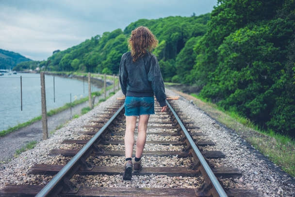 A young woman is walking on the railroad tracks - Фото, изображение