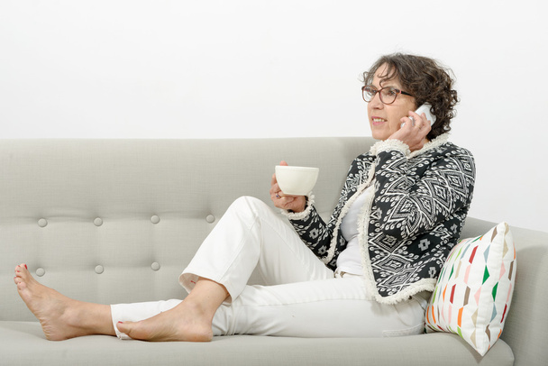 mujer madura en el sofá con un teléfono
 - Foto, imagen