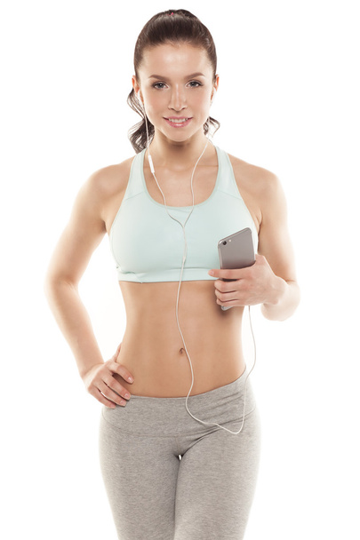 fitness meisje met een smartphone op een witte achtergrond, geniet van sport training, sportschool workout - Foto, afbeelding