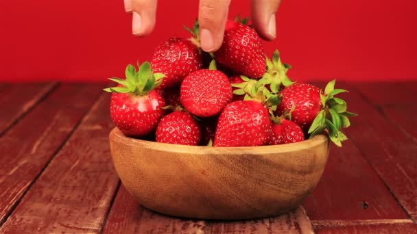 Männer Hand nehmen rote reife Erdbeere in Holzschale auf Holztisch und rotem Hintergrund - Filmmaterial, Video