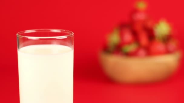 Um copo de leite e morango maduro vermelho em tigela de madeira no fundo vermelho
 - Filmagem, Vídeo