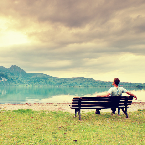 Один чоловік сидить на лавці біля блакитного гірського озера. Людина розслабляється
 - Фото, зображення