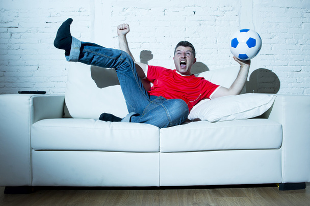 сумасшедший фанат футбола, смотрящий игру по телевизору в майке красной команды, празднующий гол
 - Фото, изображение