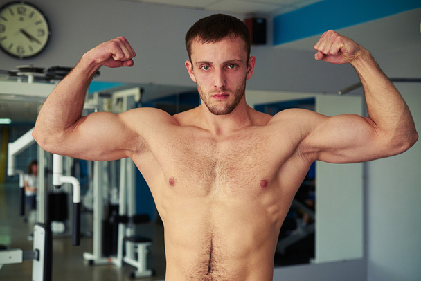 Młody człowiek mięśni, pokazując jego ciało dobrze wyszkolonych w siłowni - Zdjęcie, obraz