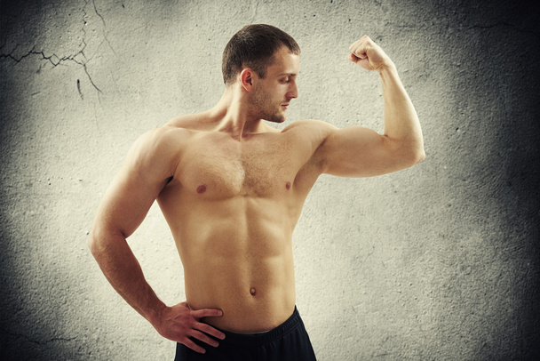 Man showing biceps on left arm over concrete wall - Фото, зображення