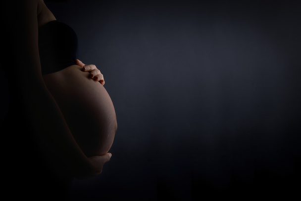 Μια έγκυος γυναίκα χαϊδεύει την κοιλιά - Φωτογραφία, εικόνα