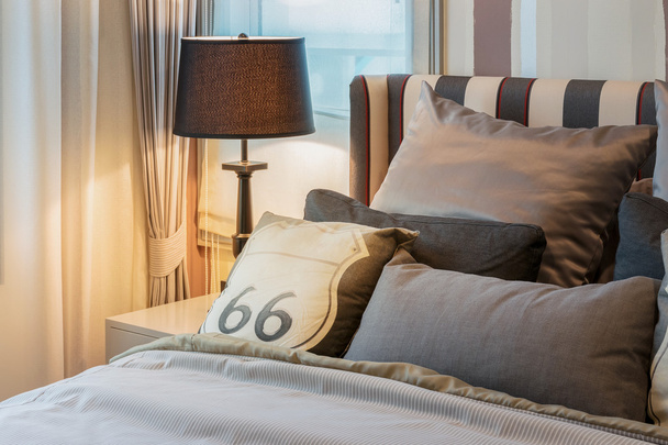 уютный интерьер спальни с темно-коричневыми подушками и лампой для чтения на тумбочке
 - Фото, изображение