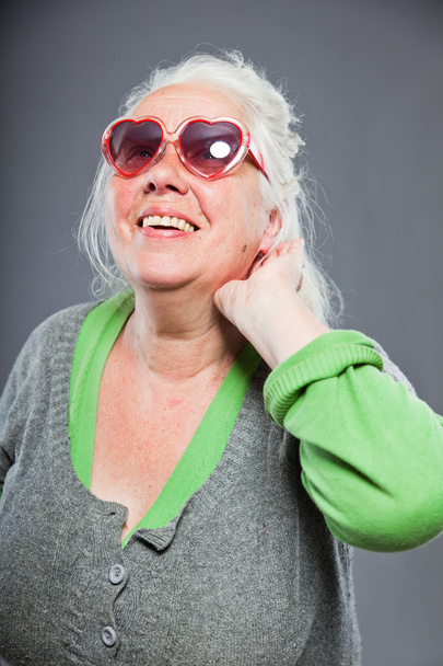 Senior woman with sunglasses deaf. Bad hearing. Hip and cool looking. Studio shot. Isolated on grey background. - Fotografie, Obrázek