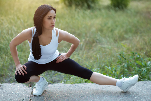 Sporty woman stretching on asphalt in park - Photo, image