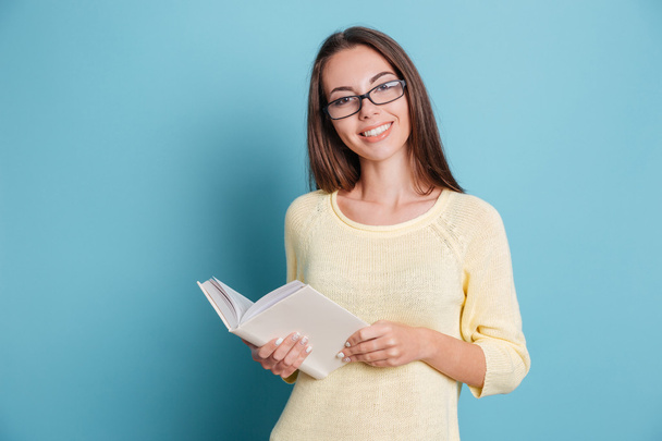 Young pretty girl with glasses holding book over blue background - Fotografie, Obrázek