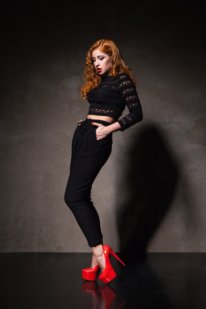 Red-haired woman posing against of black wall in light - Foto, Imagen
