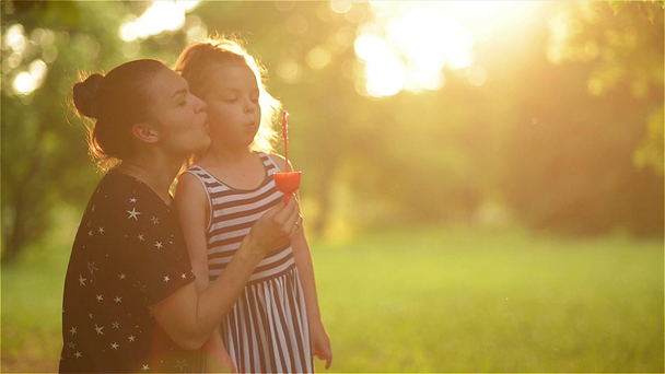 Hermosa madre con su hija en la naturaleza haciendo burbujas de jabón y riendo
 - Imágenes, Vídeo