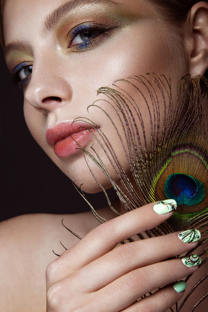 Beautiful girl with bright makeup, manicure design and peacock feather on her face. Art nails. - Photo, Image