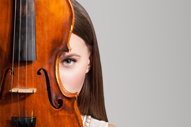 Close-up of beautiful woman looking at camera with one eye near violin - Foto, Bild