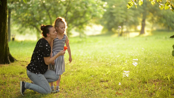 schöne Mutter mit ihrer Tochter in der Natur, die Seifenblasen macht und lacht - Filmmaterial, Video
