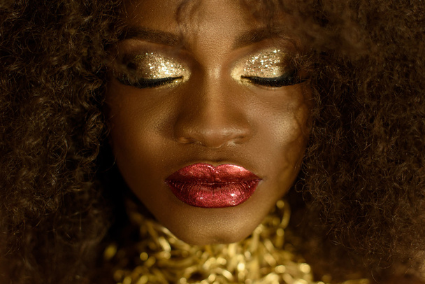 Surreal close-up portrait of young african american female model with gold glossy makeup. Face art. Fashion concept - Zdjęcie, obraz