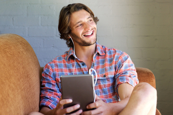 Молодий чоловік сміється вдома з цифровим планшетом
 - Фото, зображення