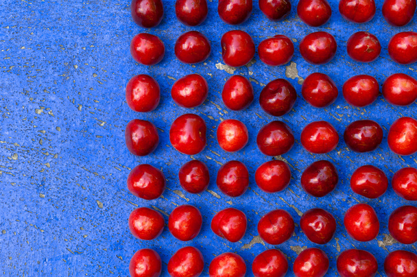 Arreglo de cerezas maduras sobre fondo textrurado azul
 - Foto, Imagen