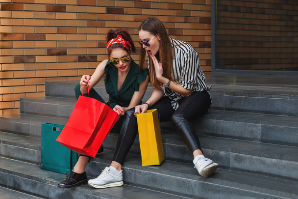 Hermosas mujeres de moda sentadas en la escalera con bolsas de compras. Estilo de vida de moda retrato urbano
. - Foto, imagen