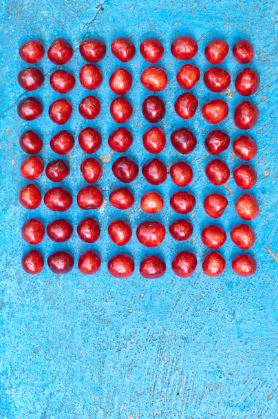 Arreglo cuadrado de cerezas maduras sobre fondo textrurado azul
 - Foto, Imagen