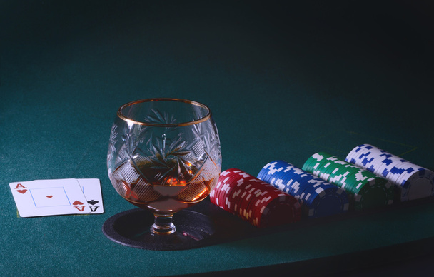 Покерный стол со стаканом коньяка, фишками казино и игральными картами. Винтажное тонированное фото
 - Фото, изображение