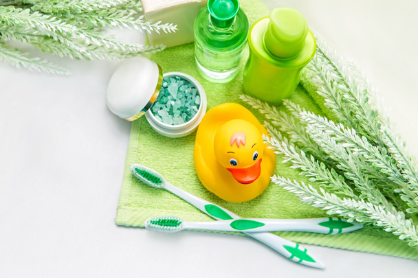 Αξεσουάρ μπάνιου σε πράσινη πετσέτα. Ελαστικό παπάκι, οδοντόβουρτσες, θαλασσινό αλάτι, σαπούνι και λοσιόν. Αξεσουάρ βρεφικής φροντίδας για μπάνιο. Παιδικό παιχνίδι με κίτρινα παπάκια. - Φωτογραφία, εικόνα