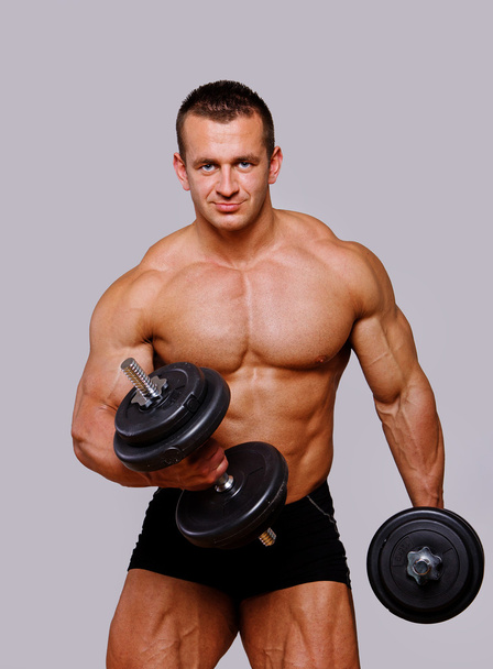Porträt eines starken Mannes, der mit Hanteln im Fitnessstudio posiert - Foto, Bild
