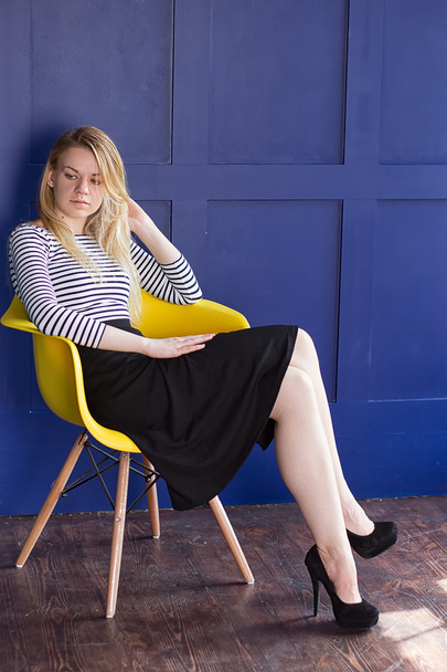 Blond girl in skirt and vest sits on a chair - Photo, Image