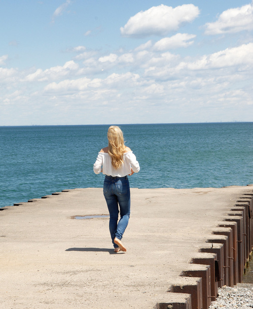 Jonge blonde vrouw lopen op een pier. - Foto, afbeelding