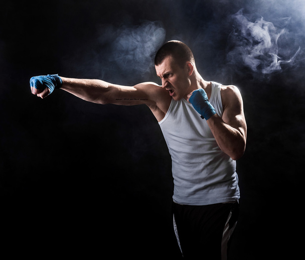 Muscular kickbox or muay thai fighter punching in smoke. - Fotoğraf, Görsel