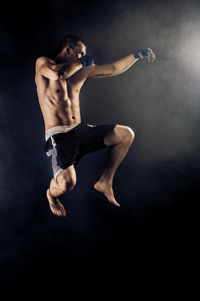 Svalnatý kickbox nebo muay thai bojovník děrování v skok. Kouř. - Fotografie, Obrázek