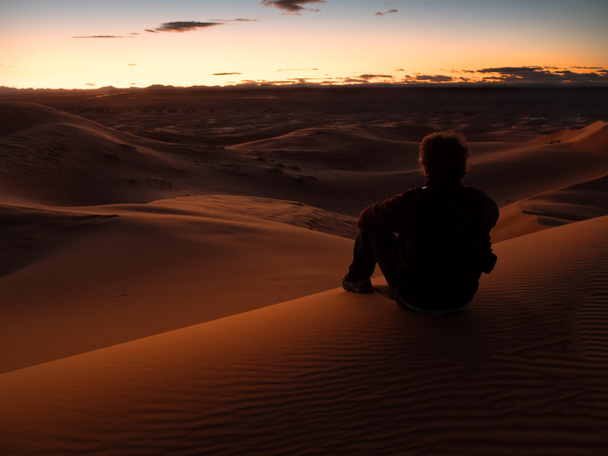 Mann sitzt auf einer Düne in der Wüste und beobachtet den Sonnenuntergang. - Foto, Bild