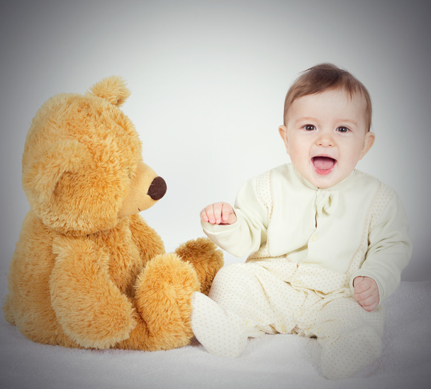 Menino bebê sentado ao lado de um ursinho de pelúcia
 - Foto, Imagem