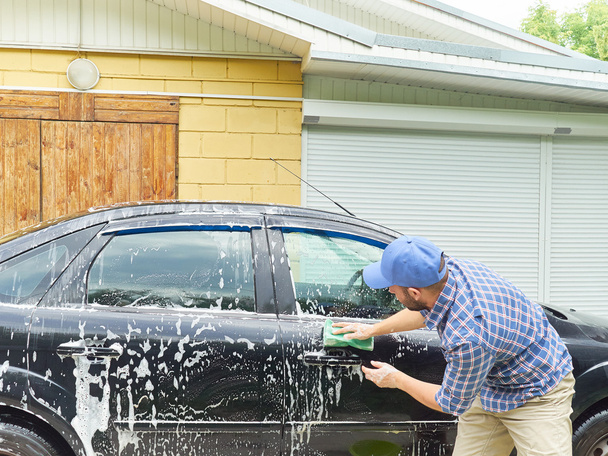 Człowiek, mycia jego czarny samochód w pobliżu house. - Zdjęcie, obraz