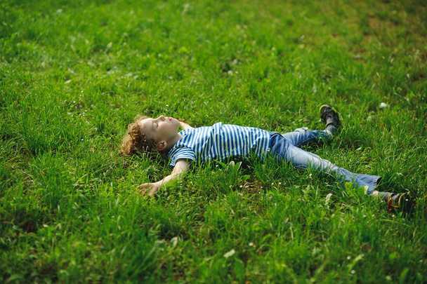 少年は芝生の上に濃い緑の草の中に横たわっている. - 写真・画像