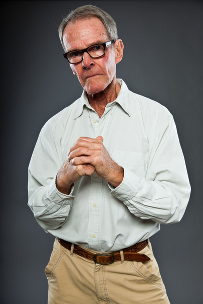 Expressive good looking senior man with glasses against grey wall. Hands praying. Spiritual and characteristic. Well dressed. Studio shot. - Photo, Image