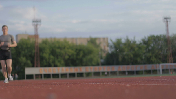 Sportowe młody facet działa na stadionie na torze wyścigowym - Materiał filmowy, wideo