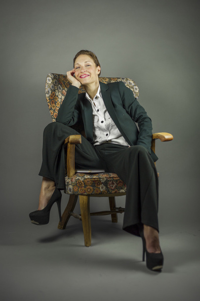 Young sensual woman in men's black suit sit in an armchair - Foto, imagen