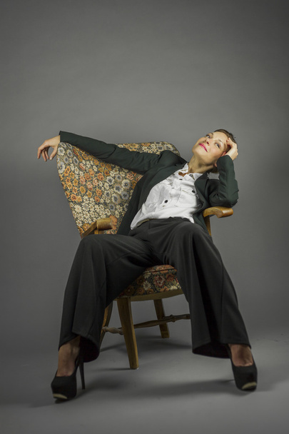 Young sensual woman in men's black suit sit in an armchair - Φωτογραφία, εικόνα