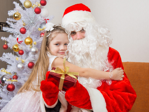 Niña abrazando a Santa Claus que está sosteniendo un regalo
 - Foto, imagen