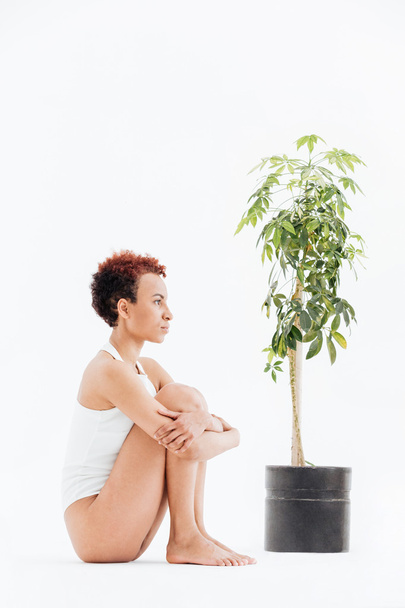 Pensive woman sitting and thinking near small tree in pot - 写真・画像
