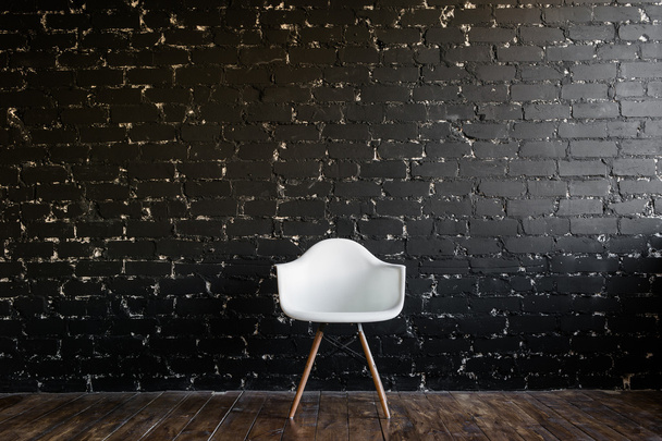 Chaise blanche debout dans la chambre sur le plancher de bois brun sur le mur de briques noires
 - Photo, image