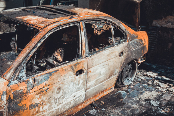 Totalmente incinerado queimado sedan luxo em um pátio pavimentado preto queimado, vista de perto através das janelas quebradas do interior enegrecido do veículo
 - Foto, Imagem