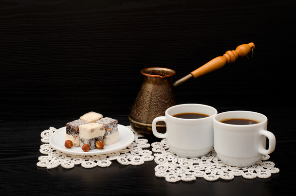 Two mugs of coffee, Turkish lokum with hazelnut, Cezve on a black background - Photo, Image