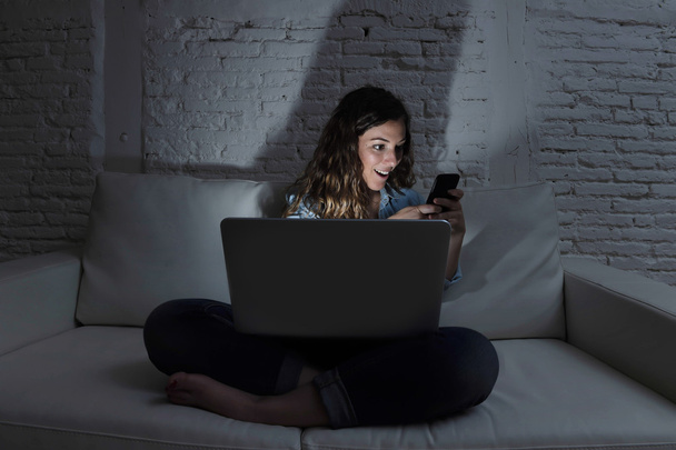 internetové sociální sítě závislá žena pomocí přenosného počítače a mobilu na gauči v noci - Fotografie, Obrázek