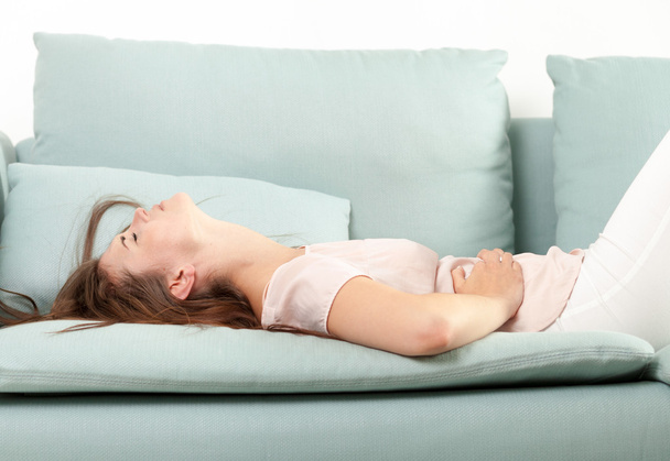 Young woman in pain lying on couch at home. Casual style indoor shoot - Foto, Imagem