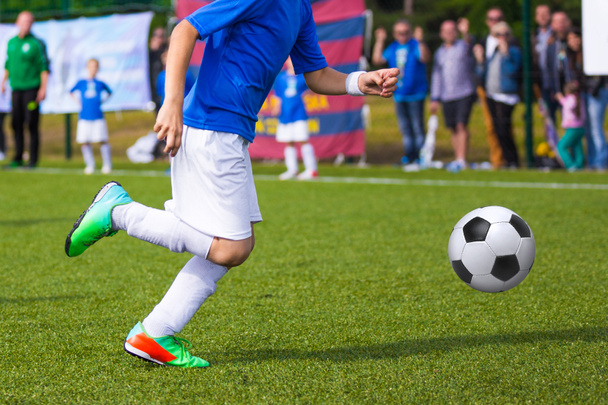 Молодой футболист пинает мяч в спортивном синем костюме
 - Фото, изображение