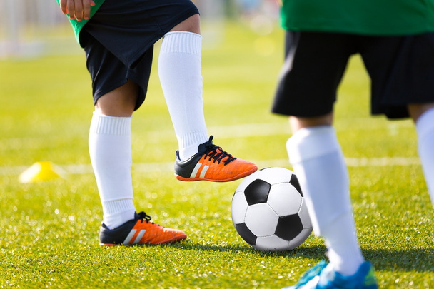 Legs feet of football player in white sports socks orange shoe and green shirt kicking soccer ball. Training session on green fresh grass for youth football soccer team. - Photo, Image